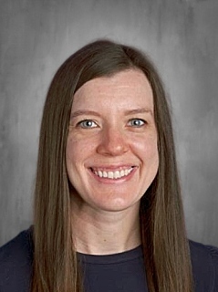 Smiling person with long brown hair against a gray background.